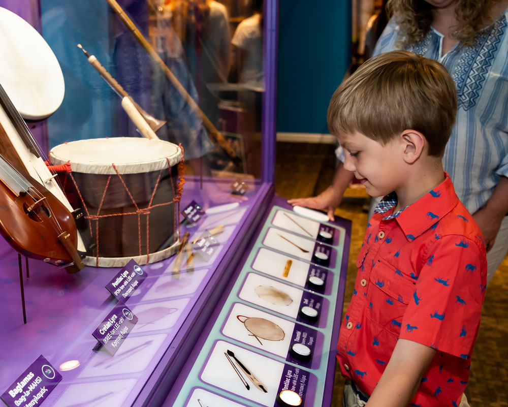 Child looking at a Greek drum on display in the Take Me There: Greece exhibit.